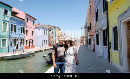 Eine lebendige Szene in Burano, Venedig, mit farbenfrohen Häusern entlang eines Kanals. Zwei Besucher posieren, um das Wesen dieser bezaubernden Insel in der V festzuhalten Stockfoto