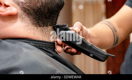Ein Friseur verwendet elektrische Schermaschinen, um in einem Friseur einen präzisen Bartschnitt zu erzielen. Die Nahaufnahme zeigt das Können und die Sorgfalt des professionellen groo Stockfoto