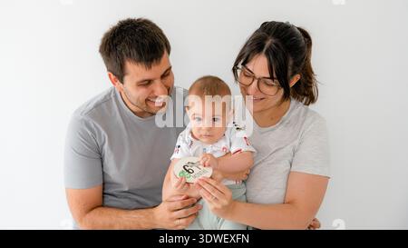 Ein fröhlicher Familienmoment mit einem fünf Monate alten Baby, das von seinen lächelnden Eltern gehalten wird. Sie sind zusammen und genießen sich in einer warmen, liebevollen Umgebung Stockfoto