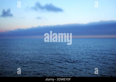 Die weite Weite des tiefblauen Meeres trifft auf den Himmel am Horizont, der mit Dämmertönen und verstreuten Wolken gemalt ist und eine friedliche Atmosphäre schafft Stockfoto