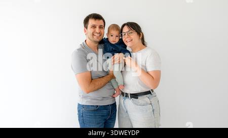 Ein liebevolles Familienporträt mit einem fröhlichen, fünf Monate alten Baby, das von seinen lächelnden Eltern gehalten wird und einen herzerwärmenden Moment der Freude und des Zusammenlebens festhält Stockfoto