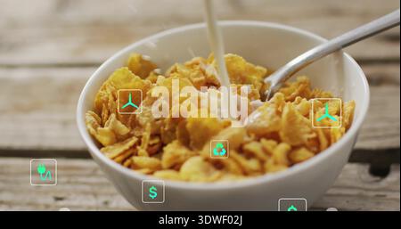 Milch in eine weiße Schüssel mit Cornflakes auf dem Tisch mit einem Metalllöffel mit türkisfarbenen Symbolen gießen Stockfoto