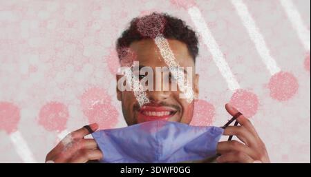 Lächelnder erwachsener Mann mit blauer Einwegmaske an schwarzen Ohrschlaufen unter dem Kinn im Studio Stockfoto