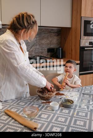 Eine Mutter und ihr Kind teilen einen besonderen Moment in der Küche und backen zusammen. Die Mutter knete Teig, während das Kind eifrig zusieht und eine Rolle hält Stockfoto