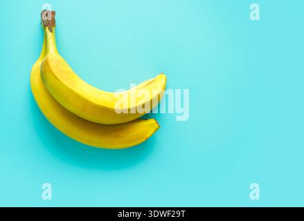 Zwei reife gelbe Bananen, die diagonal auf einem leuchtend blauen Hintergrund platziert sind, sorgen für einen auffälligen Kontrast. Die Zusammensetzung unterstreicht die Frische der Frucht Stockfoto