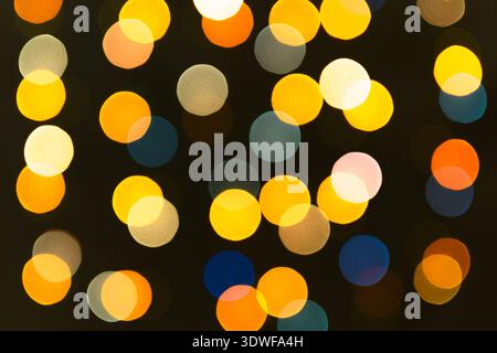 Verschwommene Lichter einer Girlande aus gelben, roten, blauen Blumen. Weihnachtliche Texturen für Dekoration und grafisches Design. Stockfoto
