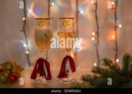 Sekt wird vor dem Hintergrund einer leuchtenden Girlande in Silvestergläser gegossen. Geringe Schärfentiefe. Stockfoto