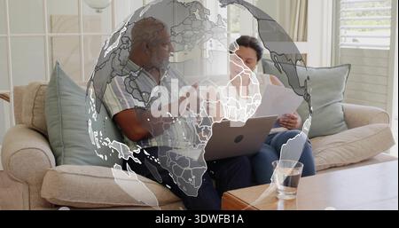 Reifes Paar zeigt auf Laptop auf beigefarbenem Sofa im Wohnzimmer, Globus-Overlay Stockfoto