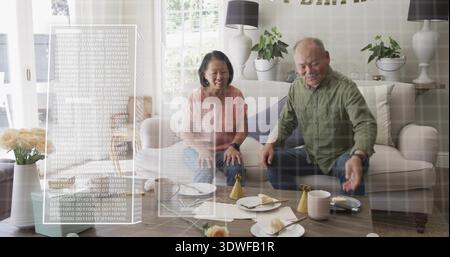 Lächelndes Seniorenpaar in lässigen Klamotten auf dem Sofa zu Hause, mit Gebäck und Hologrammen Stockfoto