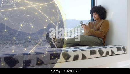 Liegender Mann in braunem Pullover, Olivenhosen auf Fenstersitz, mit Telefon, Globus-Overlay, Kopierraum Stockfoto