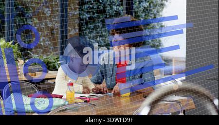 Die Betreuerin in Denim-Jacke, die sich über das Kind am Holztisch beugt und den Stift in den blauen Balken hält Stockfoto
