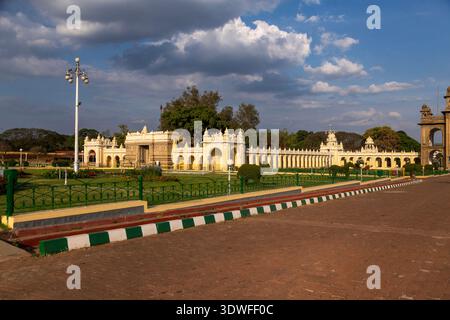 Malerischer Blick auf die verzierten Außenmauern und Gärten des Mysore Palace mit traditioneller Architektur, üppigem Grün und hellem Himmel Stockfoto