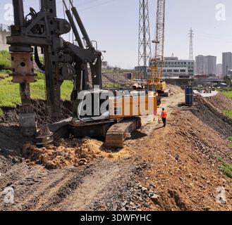 Auf einer belebten Baustelle sind leistungsstarke Kräne und schwere Maschinen in Aktion. Arbeiter in Sicherheitsausrüstung überwachen den Betrieb sorgfältig und stellen sicher Stockfoto