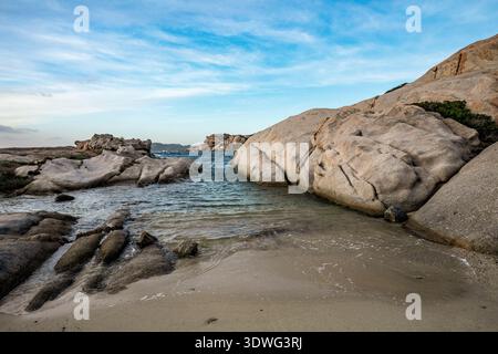Ein Blick aus der Nähe auf eine kleine Sandbucht, eingebettet zwischen majestätischen, verwitterten Granitformationen, die typisch für die Cala Francese Gegend sind. Das Bild erfasst den Stockfoto