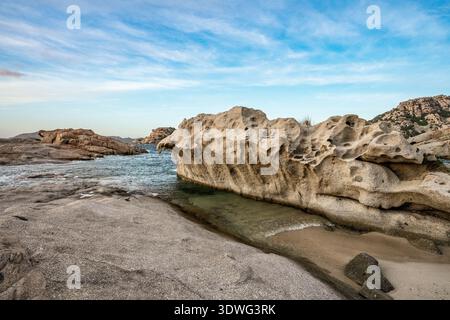Ein Blick aus der Nähe auf eine kleine Sandbucht, eingebettet zwischen majestätischen, verwitterten Granitformationen, die typisch für die Cala Francese Gegend sind. Das Bild erfasst den Stockfoto