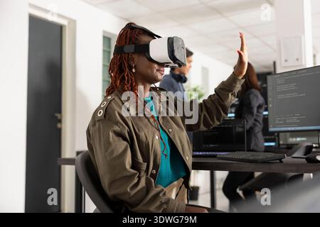 Afrikanisch-amerikanische Entwickler verwenden vr-Brillen, um die 3D-Codierungsschnittstelle zu navigieren. Black Woman arbeitet in innovativen Unternehmen, analysiert Software-Skripte und wendet virtuelle Technologien für Entwicklungsprojekte an Stockfoto