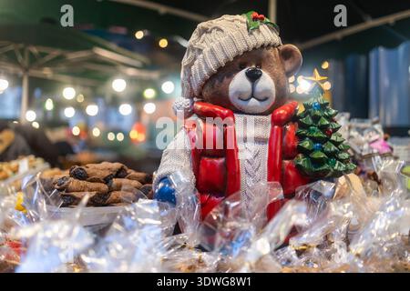 Eine große Teddybär-Figur mit Strickmütze und weihnachtsbaum an einem Marktstand mit Gebäck. Stockfoto
