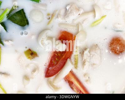 Aus nächster Nähe sehen Sie Kokos-tom-Yum-Suppe mit Huhn, Pilzen und Tomaten in einer cremigen Brühe, die frische Kräuter und leuchtende Farben zeigt Stockfoto