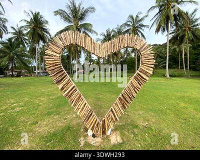 Auf grünem Gras mit Palmen im Hintergrund auf einer tropischen Insel befindet sich eine herzförmige Struktur aus Holzstäben Stockfoto