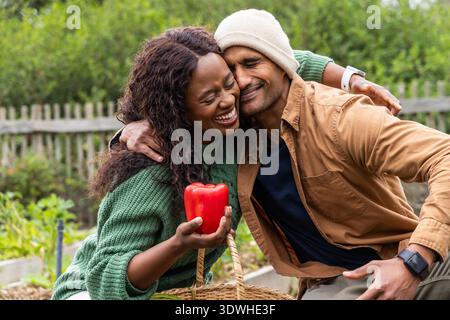 Verschiedene Pärchen sitzen im Garten, lachen, während sie roten Pfeffer halten, Frau in Pullover Stockfoto