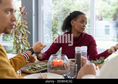 Verschiedene Pärchen essen am Tisch in der Nähe von Fenstern, Frau in kastanienbraunen Pullover Gesten, Kerze Stockfoto