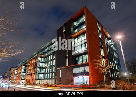 Saint Ouen, Frankreich - 9. Dezember 2025: Nächtlicher Blick auf die beleuchtete moderne Glas- und orangene Fassade des Alstom-Hauptquartiers Sigma mit Ampelpfaden in der Nähe von Paris. Stockfoto