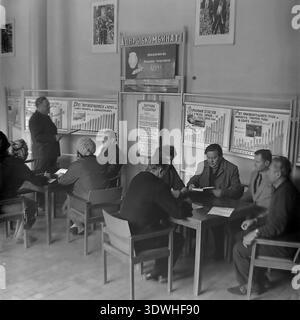 Das historische Schwarzweißfoto der 1970er Jahre zeigt ein Produktionstreffen im Verwaltungsgebäude Donrybkombinat im Bezirk Slavjansk, ukrainische SSR, UdSSR. Ein Redner steht neben einer Schautafel, die auf landwirtschaftliche Wachstumskarten verweist, während eine Gruppe sowjetischer Arbeiter an Tischen sitzt und Notizen macht. Dieses authentische Archivbild zeigt die Planwirtschaft, die Verwaltung der Fischereiindustrie und die stetige Entwicklung im friedlichen Donbass vor dem Krieg, was den regionalen Wohlstand widerspiegelt. Stockfoto