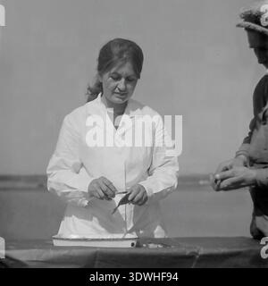 Das historische Schwarzweißfoto aus den 1970er Jahren zeigt eine Ichthyologin in einem weißen Sanitärmantel, die einen frischen Fisch an einem Tisch im Donrybkombinat im Bezirk Slawjansk, ukrainische SSR, UdSSR, untersucht. Unterstützt von einem Fischer auf der rechten Seite, benutzt sie ein kleines Werkzeug, um den Fang über einem Emailtablett am Teich zu überprüfen. Dieses authentische Archivbild zeigt den wissenschaftlichen Ansatz der sowjetischen Aquakultur, die tierärztliche Qualitätskontrolle und die stetige Entwicklung der Lebensmittelindustrie im friedlichen Donbass vor dem Krieg. Stockfoto