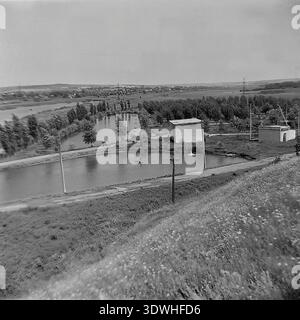 Das historische Schwarzweiß-Hochwinkelfoto aus den 1970er Jahren zeigt einen Panoramablick auf das künstliche Teichnetz und die Versorgungsgebäude im Donrybkombinat im Stadtteil Slawjansk, ukrainische SSR, UdSSR. Die Landschaft bietet Dämme, unbefestigte Straßen und kleine technische Bauten vor dem Hintergrund eines entfernten Dorfes und Hügeln. Dieses authentische Archivbild zeigt die industrielle Dimension der Aquakultur und das organisierte tägliche Leben im friedlichen Donbass vor dem Krieg, was den regionalen Wohlstand widerspiegelt. Stockfoto