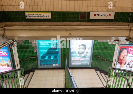London, Großbritannien, 12. Juli 2023, Treppe in der Londoner U-Bahn-Station mit gefliesten Wänden und Wegweisern. Werbeplakate sind erhältlich Stockfoto