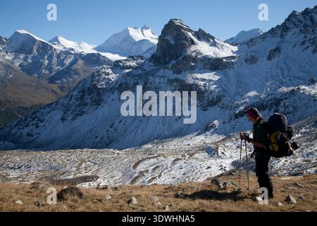 Backpacker mit einem großen Paket auf dem Wanderweg der Haute Route, der in Richtung Gruben in der Schweiz absteigt. Stockfoto