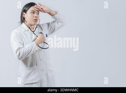 Junge Ärztin, die ihren eigenen Herzschlag mit Stethoskop hört. Asiatische Ärztin hört ihren eigenen Herzschlag mit Stethoskop isoliert Stockfoto