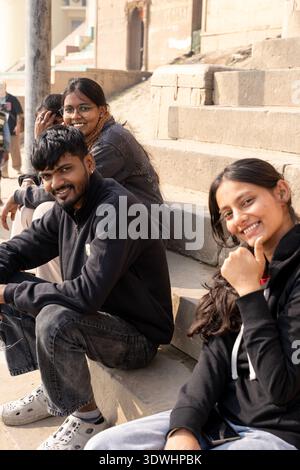 Lächelnde junge Erwachsene sitzen auf Steintreppen und genießen einen sonnigen Tag in Varanasi, Indien. Stockfoto