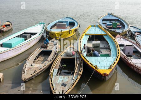 Eine Gruppe von bunten Holzbooten legte am Fluss an, mit Menschen, die sie in Varanasi, Indien, vorbereiteten. Stockfoto