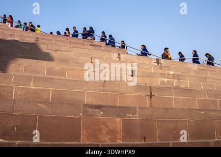 Gruppe von Menschen, die an einem sonnigen Tag in Varanasi, Indien, über breite Steintreppen mit Metallgeländer spazieren. Stockfoto