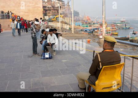 Ein Sicherheitsbeamter überwacht eine Gruppe von Menschen, die in der Nähe des Ufers in Varanasi, Indien, sitzen und gehen. Stockfoto