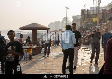 Die Menschen treffen sich und spazieren an einer belebten Uferpromenade in Varanasi, Indien, bei Tageslicht. Stockfoto