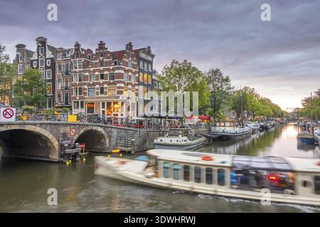Niederlande. Wolkig Dämmerung auf dem Amsterdamer Kanal. Hausboote und Boote sind vertäut. Reflexion im Wasser der traditionellen Häuser und einer Brücke Stockfoto