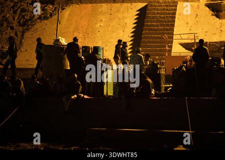 In Varanasi, Indien, versammeln sich Menschen mit Silhouetten in der Nähe von beleuchteten Stufen und schaffen eine warme, atmosphärische Szene. Stockfoto