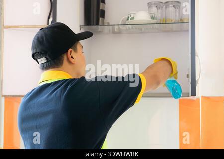 Professioneller männlicher Reiniger, der moderne Küche desinfiziert, Arbeitsplatten und Geräte abwischt Stockfoto