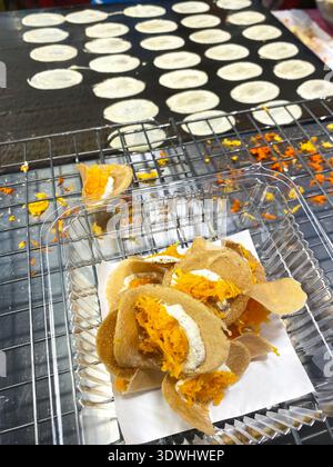 Traditionelles thailändisches Streetfood bietet Kokospankuchen gefüllt mit süßen Toppings, wobei der Kochprozess an einem Marktstand in Thailand deutlich wird Stockfoto