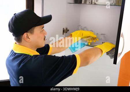Professioneller männlicher Reiniger, der moderne Küche desinfiziert, Arbeitsplatten und Geräte abwischt Stockfoto
