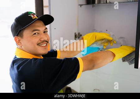 Professioneller männlicher Reiniger, der moderne Küche desinfiziert, Arbeitsplatten und Geräte abwischt Stockfoto
