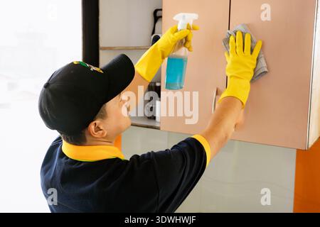 Professioneller männlicher Reiniger, der moderne Küche desinfiziert, Arbeitsplatten und Geräte abwischt Stockfoto