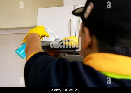 Professioneller männlicher Reiniger, der moderne Küche desinfiziert, Arbeitsplatten und Geräte abwischt Stockfoto
