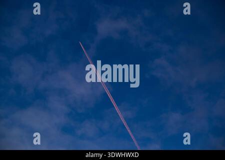 Leuchtend orangefarbener Kondensstreifen teilt einen tiefblauen Abendhimmel mit weichen Wolken Stockfoto