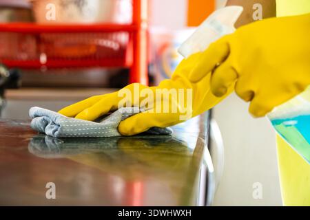 Professioneller männlicher Reiniger, der moderne Küche desinfiziert, Arbeitsplatten und Geräte abwischt Stockfoto