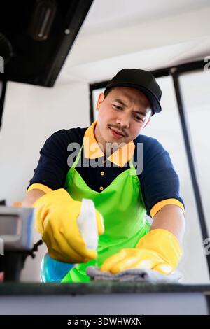 Professioneller männlicher Reiniger, der moderne Küche desinfiziert, Arbeitsplatten und Geräte abwischt Stockfoto