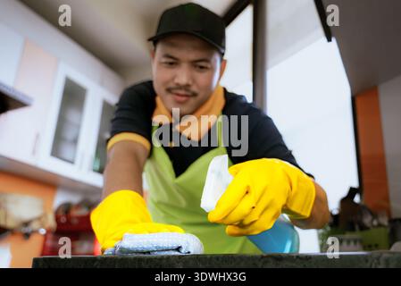 Professioneller männlicher Reiniger, der moderne Küche desinfiziert, Arbeitsplatten und Geräte abwischt Stockfoto