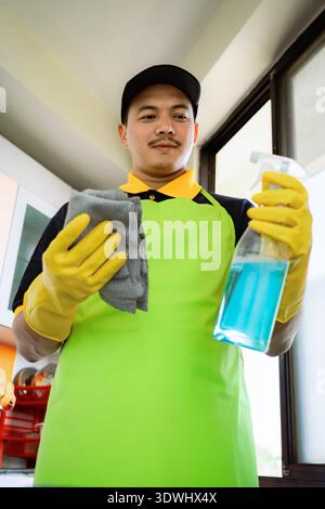 Professioneller männlicher Reiniger, der moderne Küche desinfiziert, Arbeitsplatten und Geräte abwischt Stockfoto
